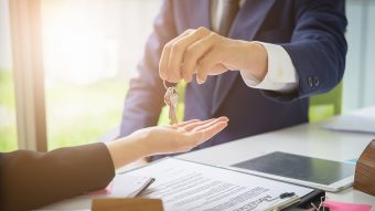 Agents are giving house keys of customer and holding dollar us bank at agency office. Agreement and real estate concept.